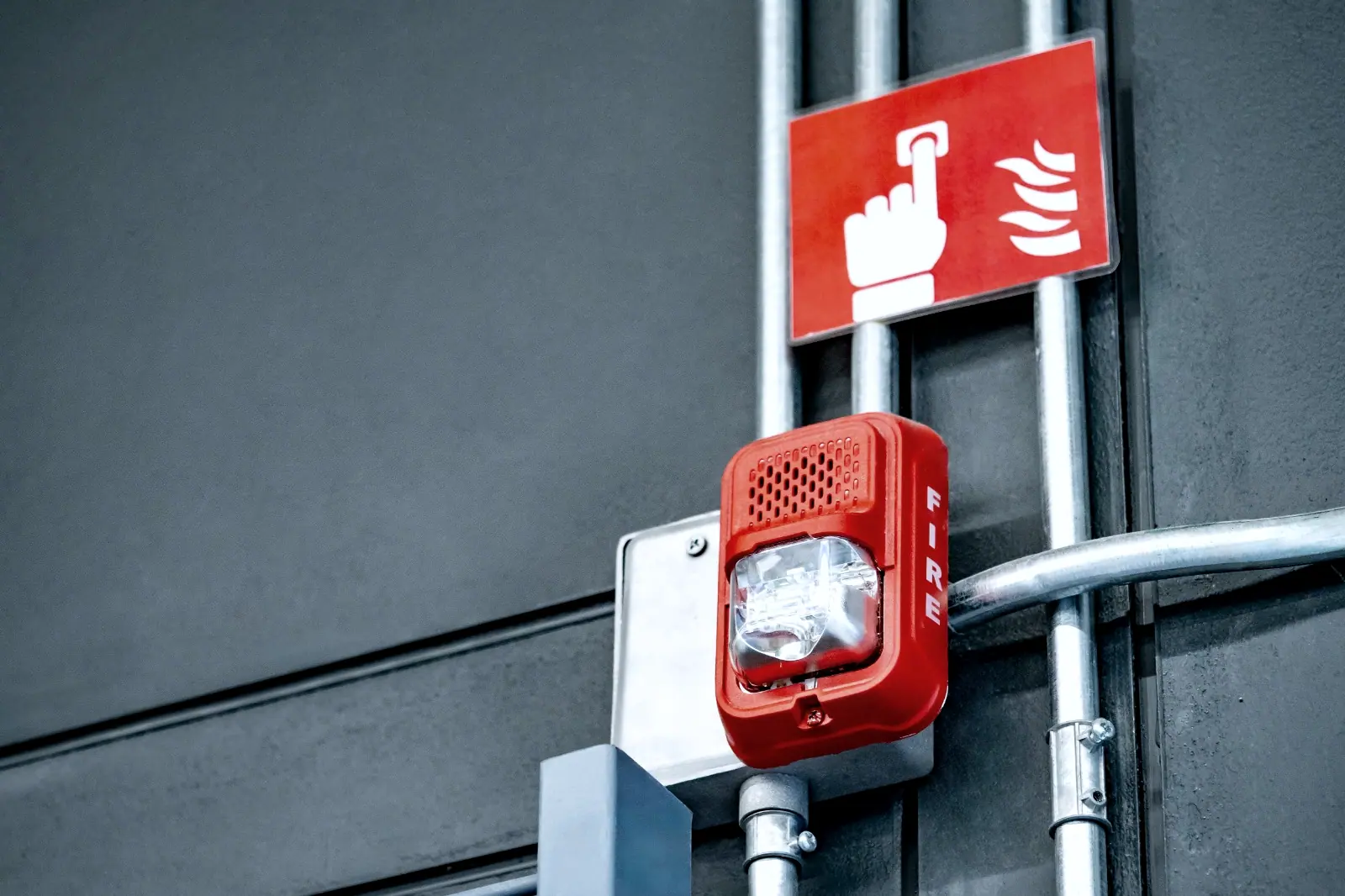 Fire alarm strobe and manual call point installed on a wall beside metallic conduits